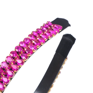 Close-up of pink teardrop rhinestones on a black headband with golden metal settings