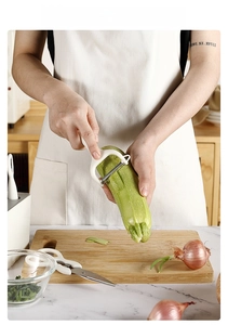 Detail of white stainless steel peeler and kitchen shears in use with fresh vegetables
