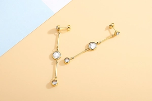 Detail of long gold tassel earrings featuring three graduated clear zircons on bicolored background