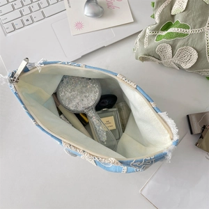 Light blue cosmetic bag with lace flower and tassels shown holding skincare products