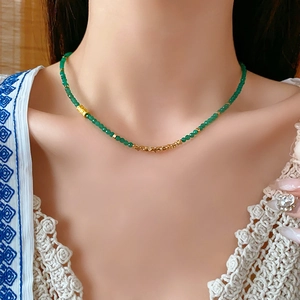 Gros plan d'un collier de perles vertes et dorées porté sur le cou d'une femme