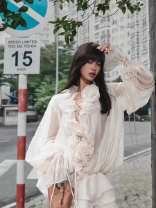 Detail of white ruffle blouse with 3D floral decorations and lace-up front detail