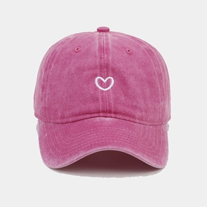 Detail of heart embroidery on washed magenta cotton baseball cap with vintage finish