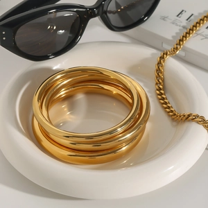 Set of thick 18k gold plated stainless steel bangles with polished finish on ceramic tray