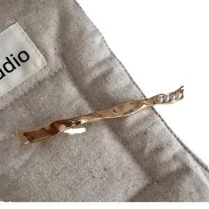 Elegant gold metal wave hair clip with four small pearls on a minimalist linen background