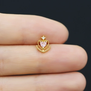 Macro detail of gold piercing stud with pink heart stone and white zircon accents