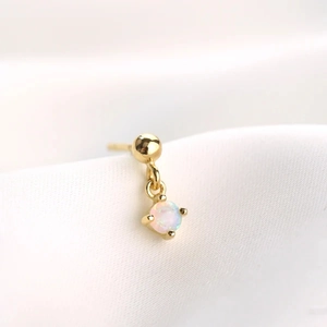 Macro detail of a single gold stud earring with a prong-set iridescent opal stone