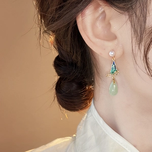 Close-up of pearl earrings with blue enamel mountains and a green teardrop jade pendant