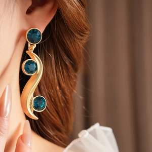 Close-up of vintage gold wavy earrings with three sparkling blue gemstones on model