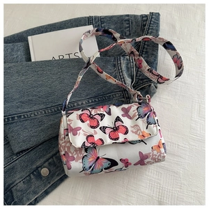 Close-up of white butterfly print crossbody bag on denim jacket and white book