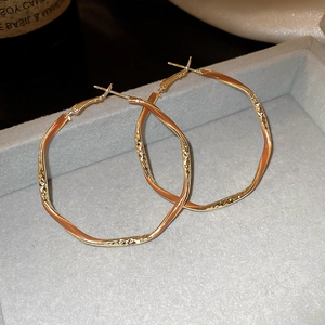 Detail of gold oversized hoop earrings with irregular wave texture on grey velvet background