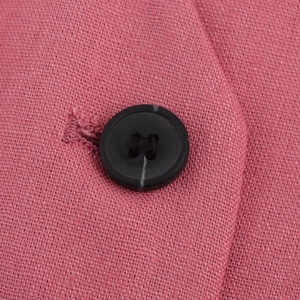 Close-up of a black four-hole button on pink woven fabric for a British vest suit