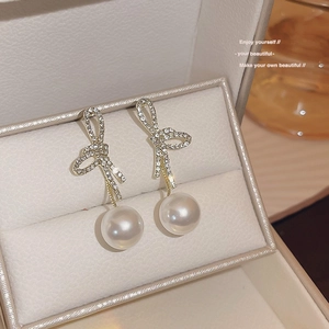 Macro shot of elegant bow earrings with rhinestones and pearls in a cream jewelry box