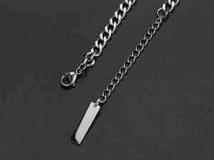 Detail of silver Cuban chain necklace with a polished rectangular tag on a black background