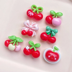 Flat lay of mini resin red cherries with bows and smiley faces for DIY crafts