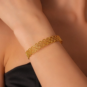 Detail of gold-colored geometric hollow flower pattern cuff bracelet on woman's wrist