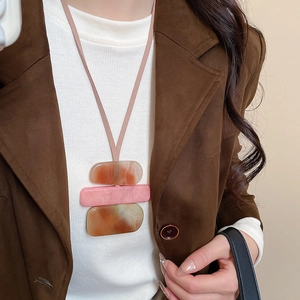 Detail of acrylic geometric square pendant necklace styled with a brown velvet blazer
