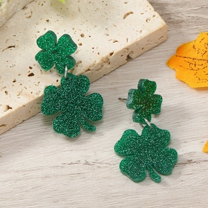 Detail view of St. Patrick's Day green glitter shamrock earrings on a stone background