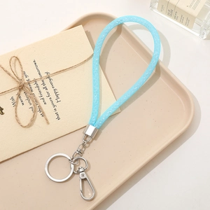 Close-up of a light blue glitter strap keychain with silver spring ring on a tray