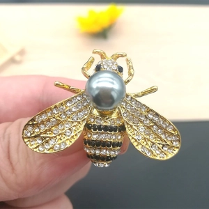 Detailed view of a golden bee brooch with sparkling crystals and a grey pearl inlay