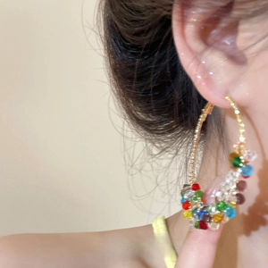 Close-up of large gold hoop earrings with multi-colored beads worn by a female model
