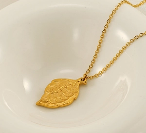 Macro shot of gold leaf pendant with embossed texture on minimalist white plate