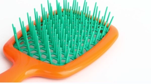 Close-up of orange and green hollow honeycomb hairbrush with vented design for fast drying