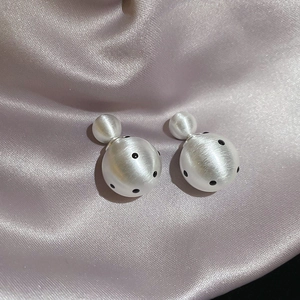 Detailed macro view of 18k gold plated earrings with white black dots on purple silk