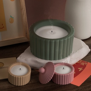 Trois bougies à rayures en vert, beige et rose posées sur une table en bois foncé
