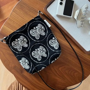 Detail of black canvas crossbody bag with white butterfly embroidery and simple wish label