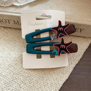 Detail of star-shaped hair clips with m-letter logo on a Fashion Jewelry card