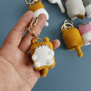 Handmade yellow crochet cat keychain with golden ring held against a blue background