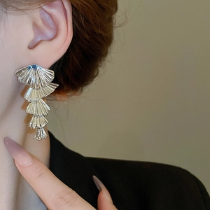 Close-up of fan-shaped silver drop earrings with metallic texture on model's ear