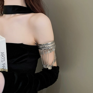 Detail view of silver arm cuff with coin pendants and hanging tassel chains on model