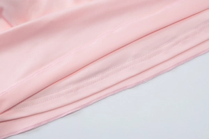 Detailed close-up of pink jersey fabric showing professional double-needle stitching and hem