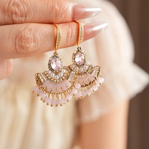 Gros plan de boucles d'oreilles éventail dorées avec gemmes roses, perles et glands