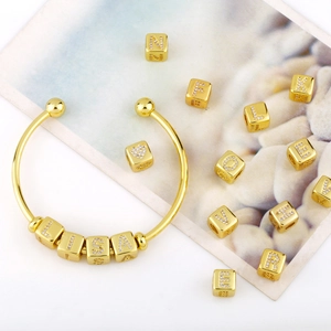 Close-up of gold-plated open bangle with customizable diamond-encrusted letter beads