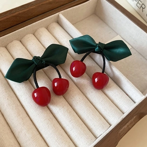 Green satin bow hair clips with red resin cherries displayed in a wooden jewelry box