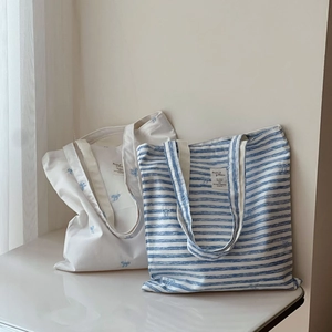 Blue and white striped canvas tote bags with bow embroidery in a minimalist setup