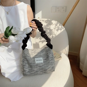 Detail of textured woven shoulder bag with ruched strap and stylish white fabric label