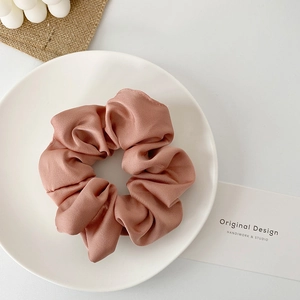 Detailed close-up of a dusty rose satin scrunchie on a decorative white porcelain plate