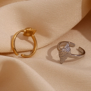 Macro shot of 18K gold and silver shell-shaped rings on soft beige fabric texture