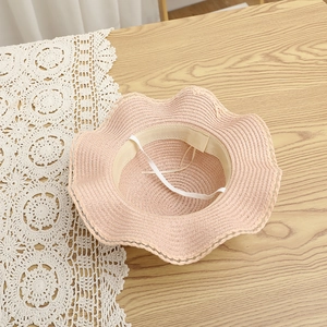 Detailed top view of pink straw sun hat with ruffled brim and adjustable chin strap