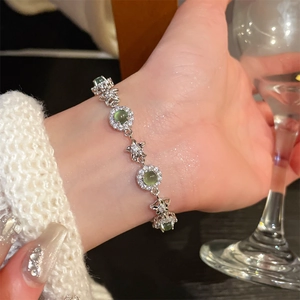 Detail of silver flower bracelet with green gemstones and white zircons on woman's wrist