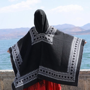 Vue détaillée d'un poncho noir à capuche avec motifs de cœurs blancs et de longs franges