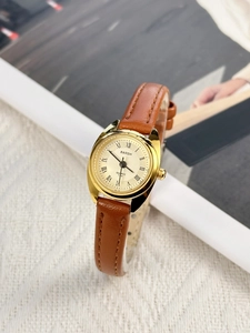 Detailed close-up of a women's watch with an oval gold case and brown leather strap