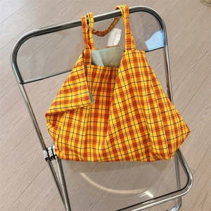 Detail of checkered canvas tote bag hanging on chair with yellow plaid and wide handles