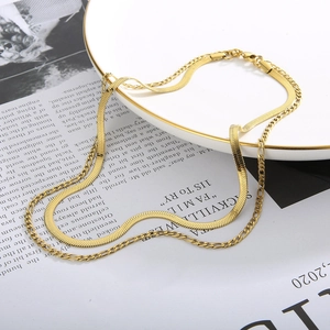Detail of layered gold necklaces with flat snake chain and Figaro link on white plate