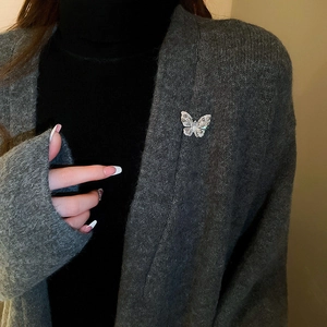 Detailed close-up of a silver butterfly brooch with teardrop zircon on a grey sweater