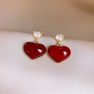 Gros plan de boucles d'oreilles cœur rouge avec clous dorés sur tissu de satin